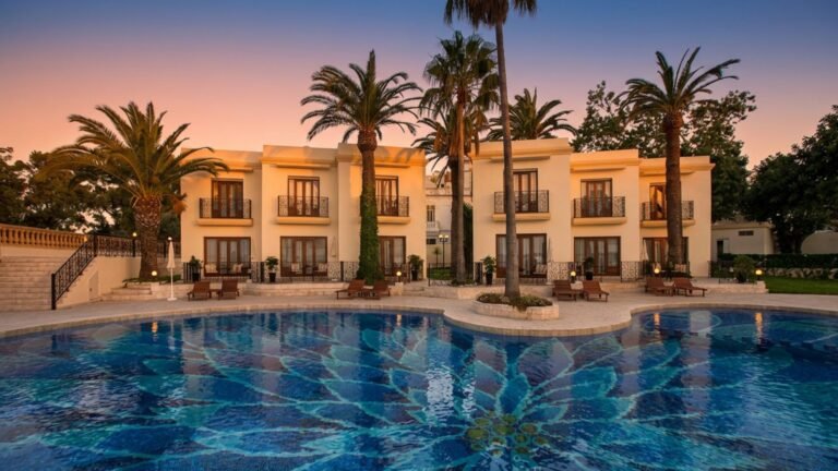 Série vacances en septembre – Le Grand Hôtel Villa de France Tanger : Notre quatrième escale chargée d’histoire Vue sur la piscine entourée de palmiers et de végétation lors d'un crépuscule à la Villa de France Tanger.