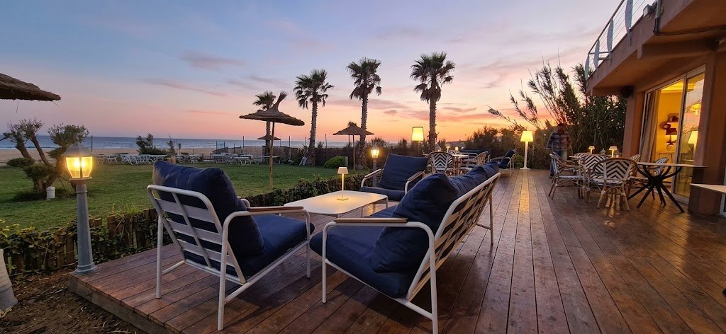 La terrasse en bois du restaurant KD.Signature by La piscine à Tanger face à l'Océan Atlantique, lors d'un coucher de soleil aux teintes crépusculaires.