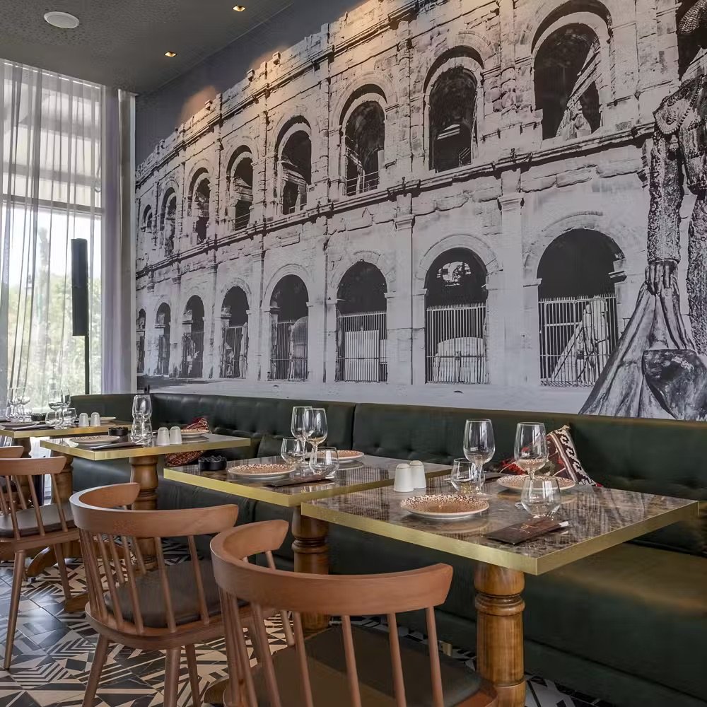 Espaces événementiels de style restauration avec des tables dressées et une grande fresque murale d'arènes romaines.