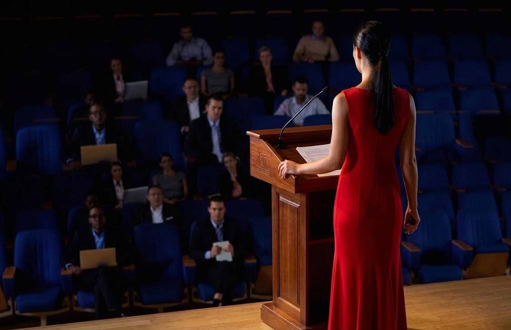 Une conférencière en robe rouge s'exprime derrière un pupitre en bois devant un auditorium de congrès à Tanger.