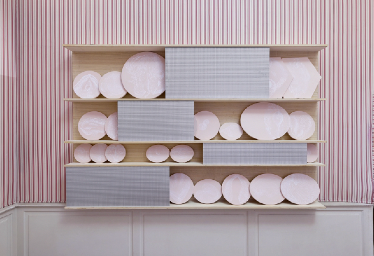 Installation d'art contemporain représentant un dressoir en bois rempli d'assiettes et disques roses sur fond de papier peint à rayures par Ghislaine Portalis à la Galerie Delacroix à Tanger
