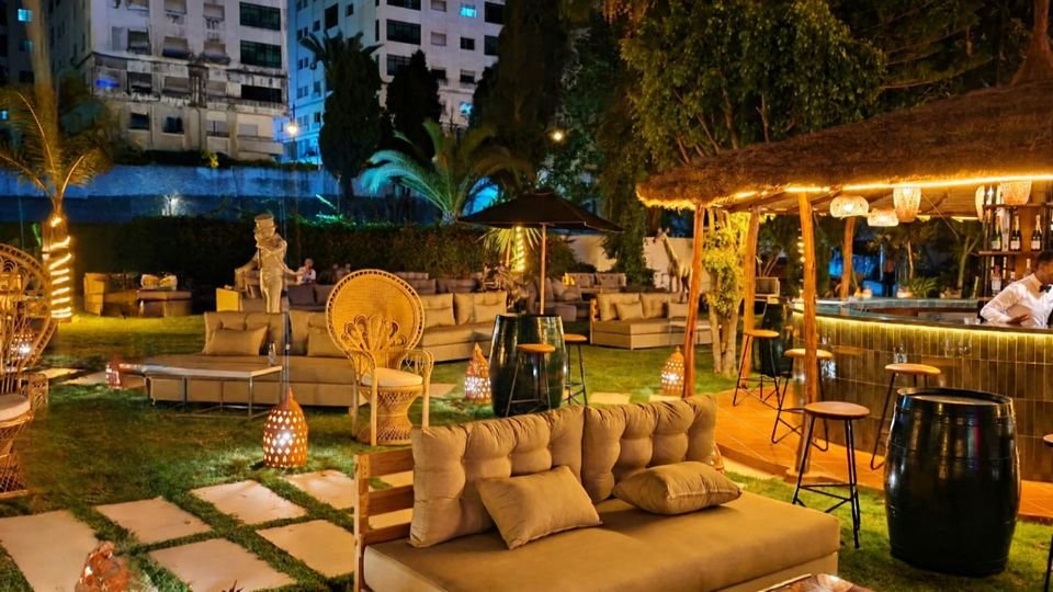 Salons extérieurs éclairés de nuit avec bar en paille sous les palmiers, un espace des restaurants de l'hôtel 