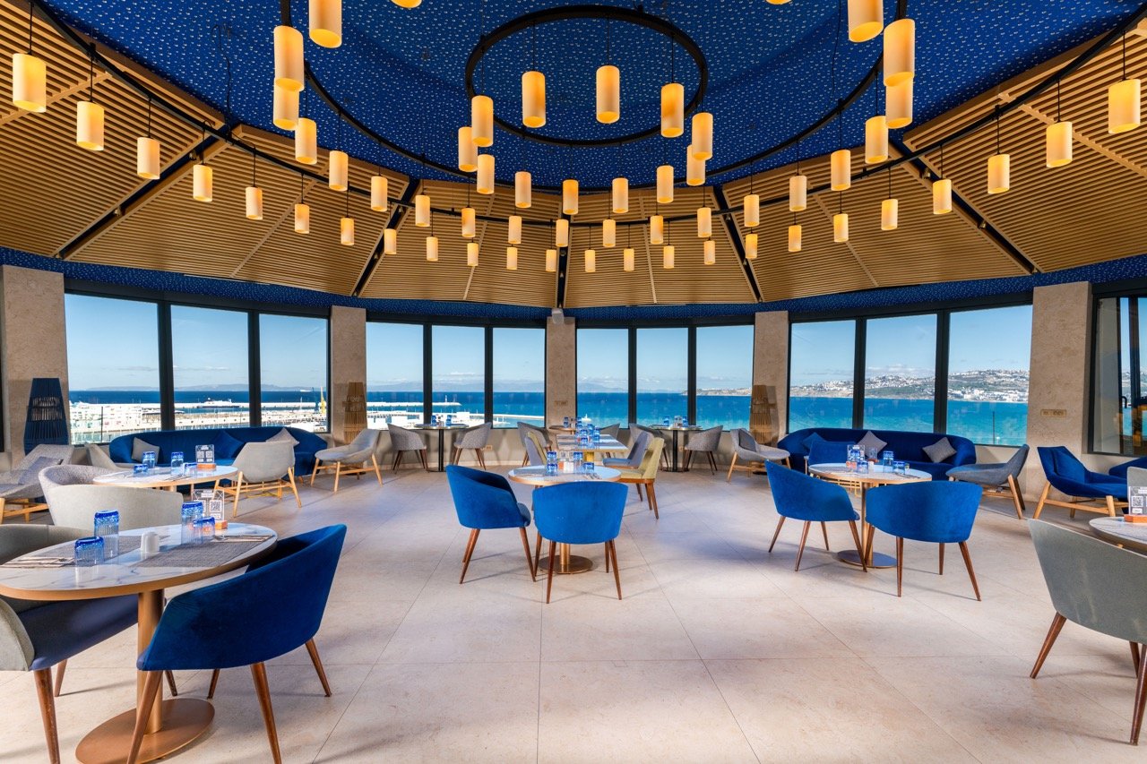 Salle intérieure au design moderne et feutré du B-Heaven Rooftop avec baies vitrées sur la mer.